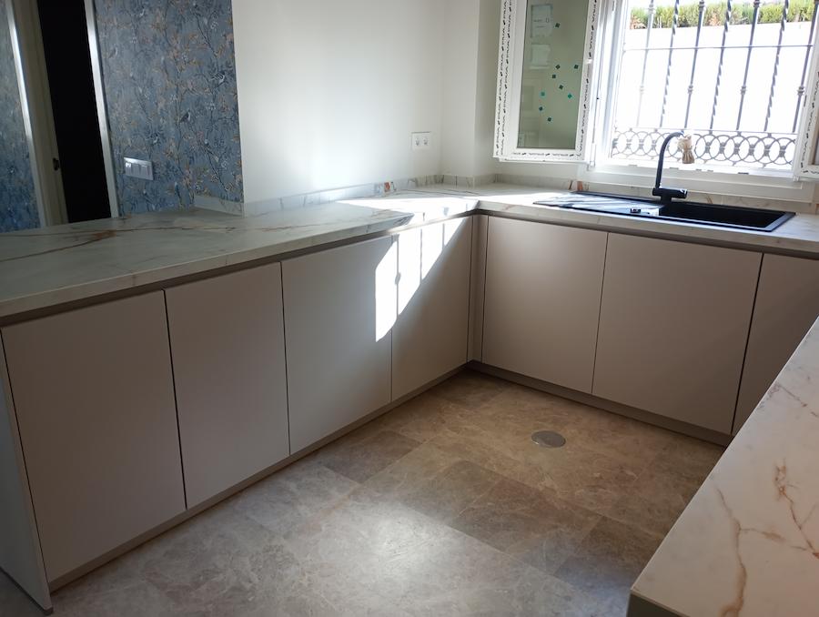 Cocina en U con muebles bajos sin tiradores, encimera de porcelánico y fregadero negro montado bajo la ventana.